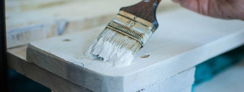 Une personne qui applique de la peinture blanche sur du bois avec un pinceau